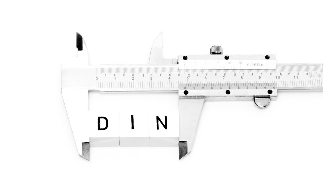 Ein Messschieber mit umklammerten Buchstaben auf denen DIN geschrieben steht.